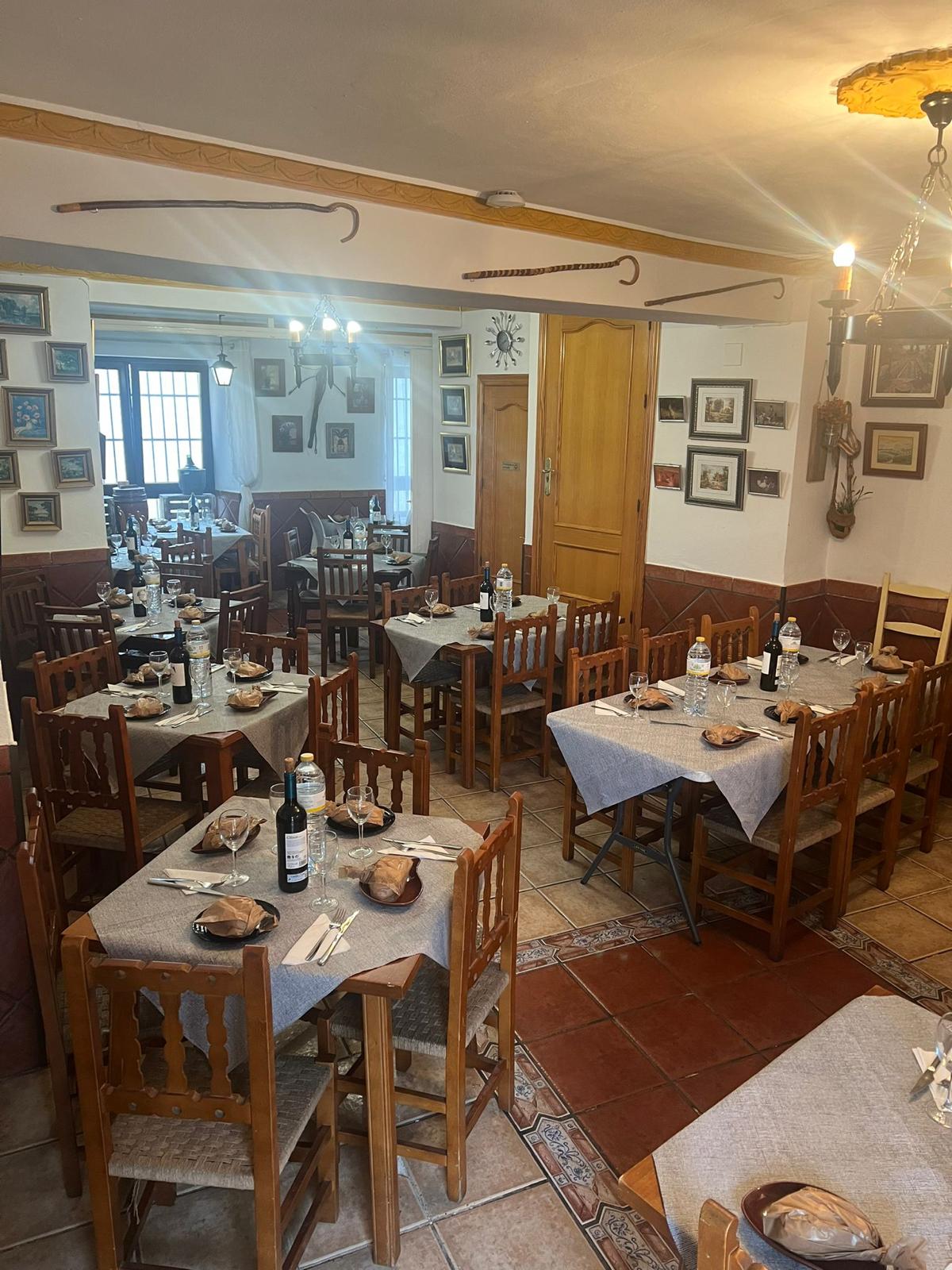 Salón encalado con mesas de madera y cuadros en las paredes