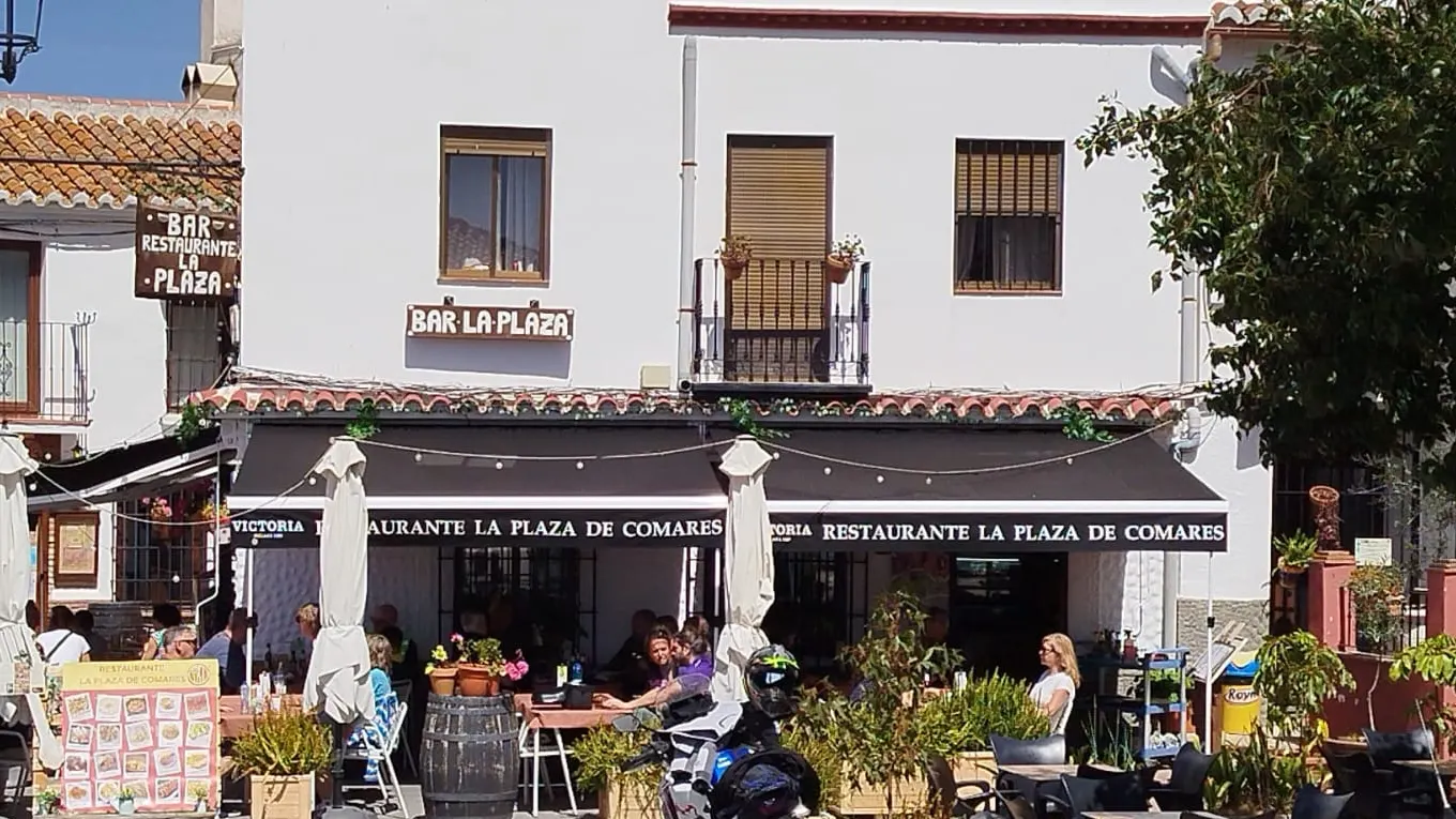 Fachada del bar La Plaza con su toldo negro y la terraza en la plaza de Comares